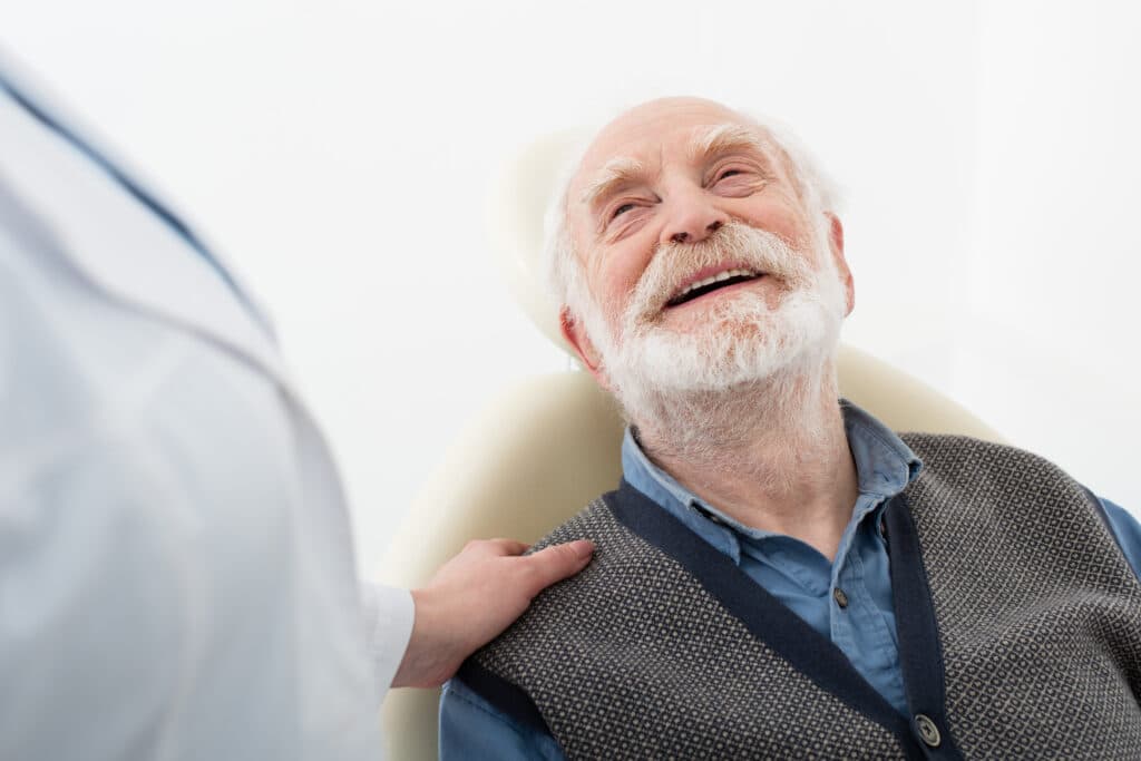 Smiling Senior Patient Sitting In Dental Chair With Dentist Hand